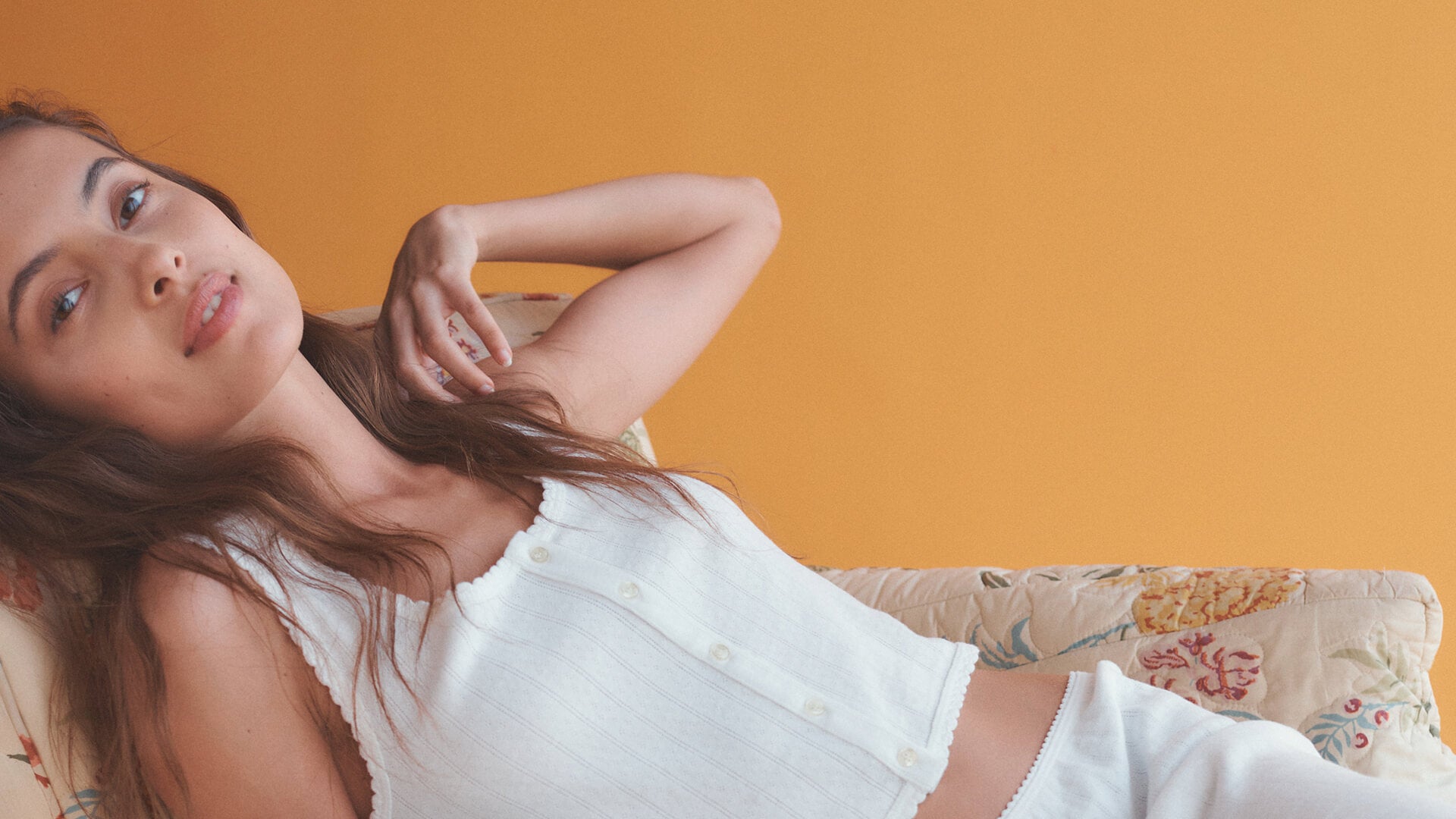 Close up of woman laying on couch in white Pointelle tank with arm up.