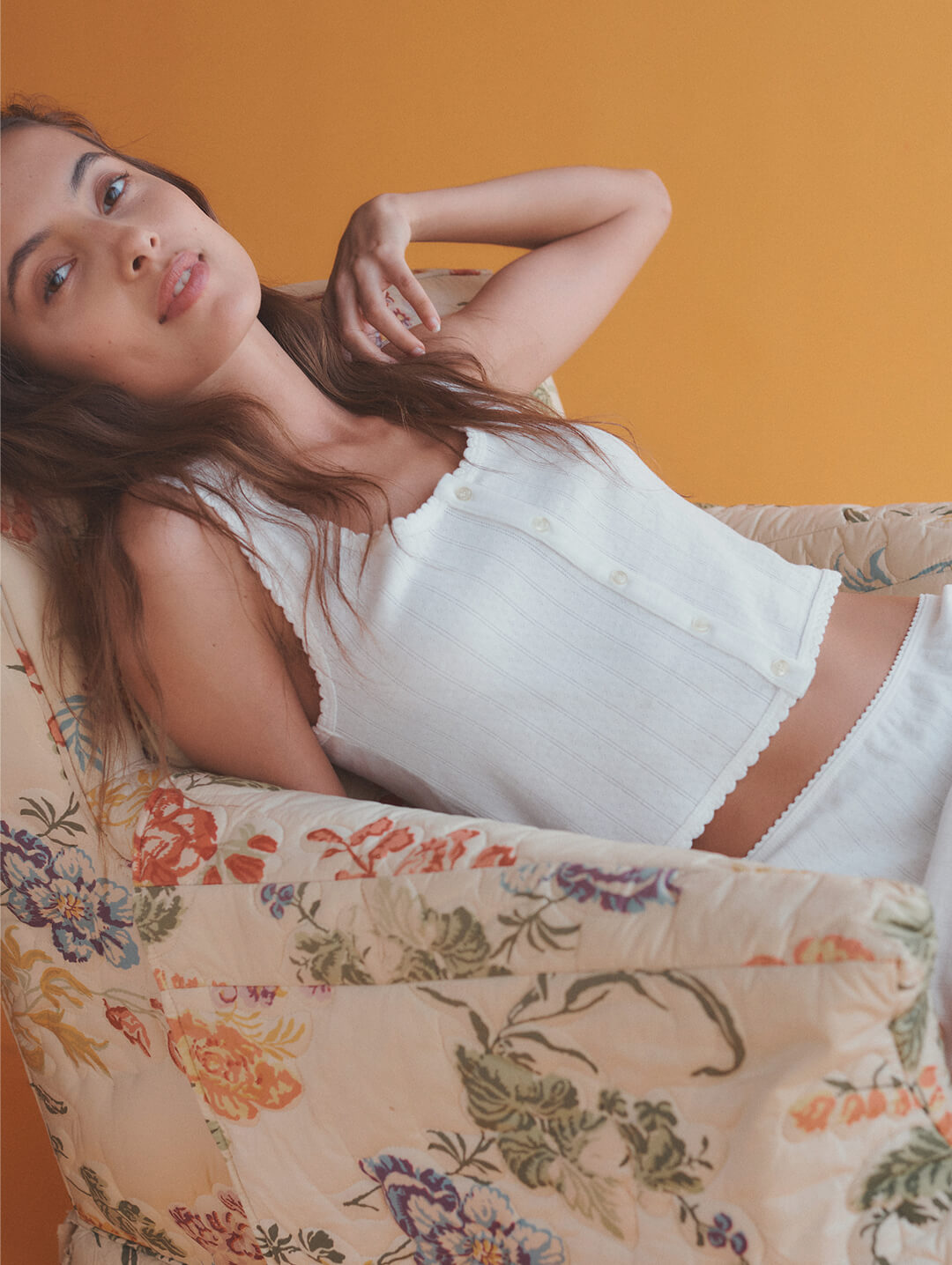 Close up of woman laying on couch in white Pointelle tank with arm up.