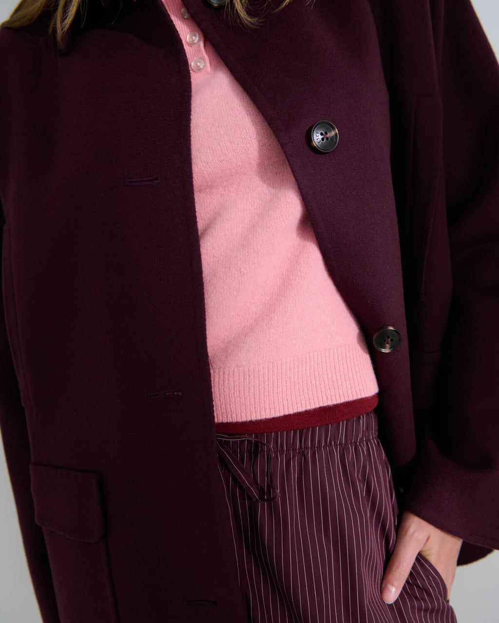 Close up zoom of Noah bordeaux jacket layered over Jesse rose polo, and Yoshi striped bordeaux pants, with hand in pocket.