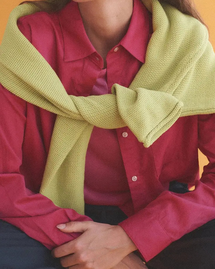 Close up of bright pink button down, with green sweater draped over.