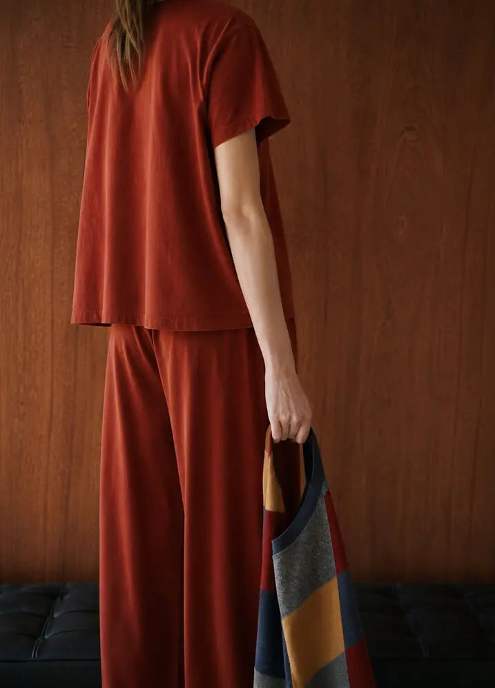 Back of model wearing rust colored tshirt and pants holding sweater