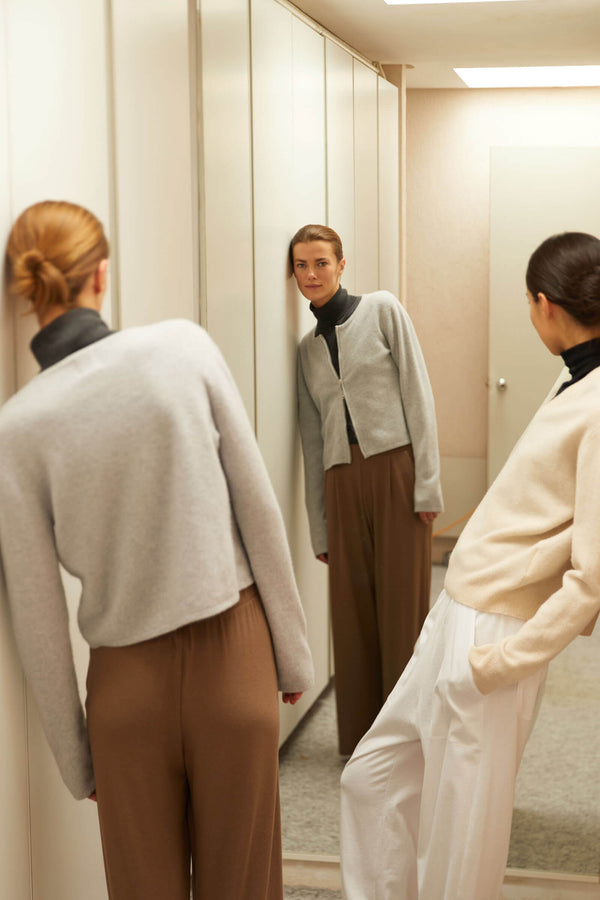 Two women leaning against walls in sweaters and pants