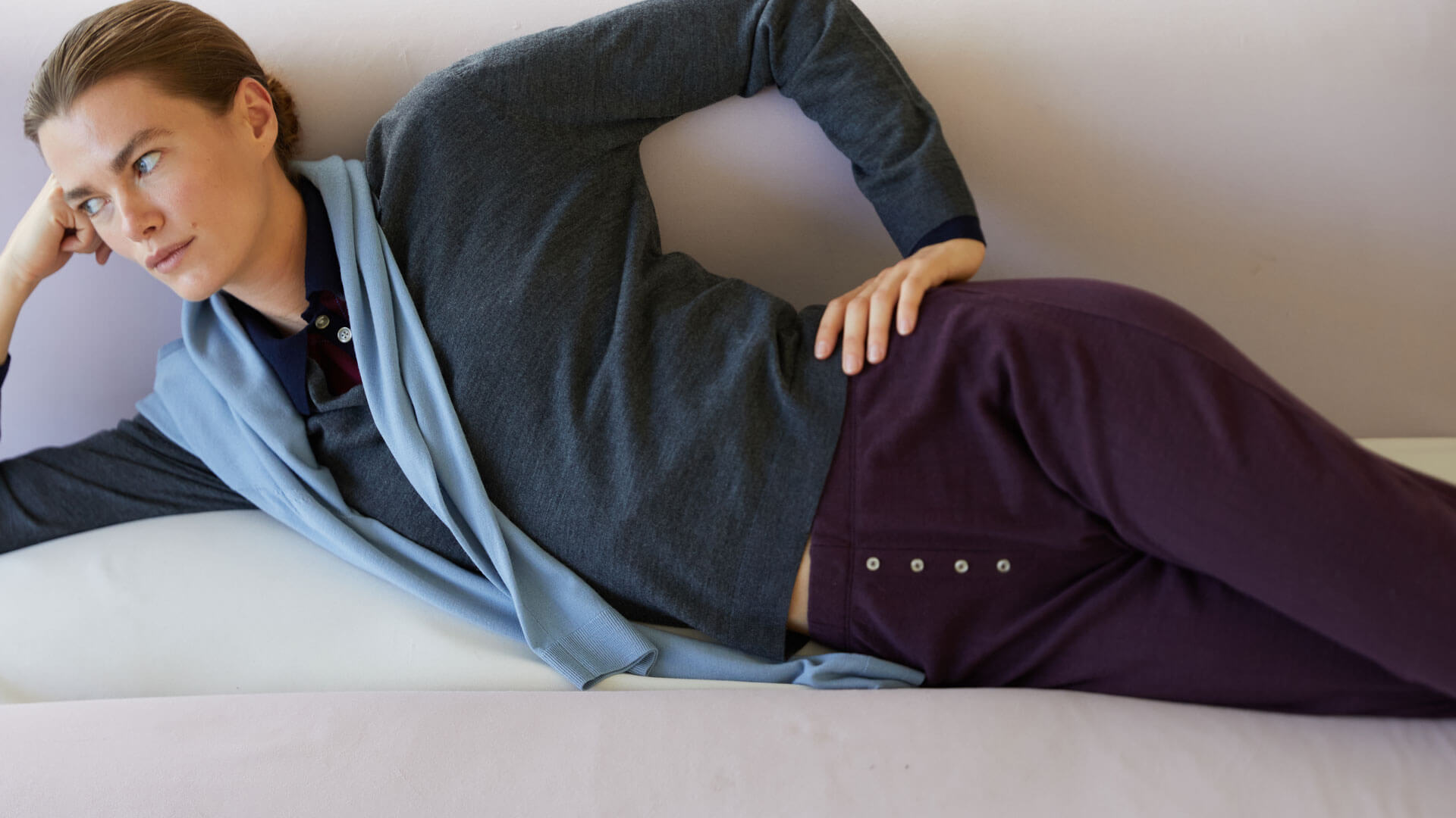 Woman laying on couch in berry Pointelle and layered James sweaters, looking into distance