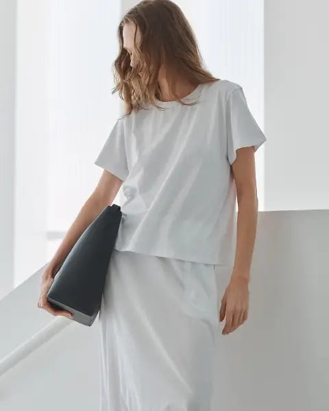 Woman leaning to the side in white Margo t-shirt with black back, and white maxi skirt.