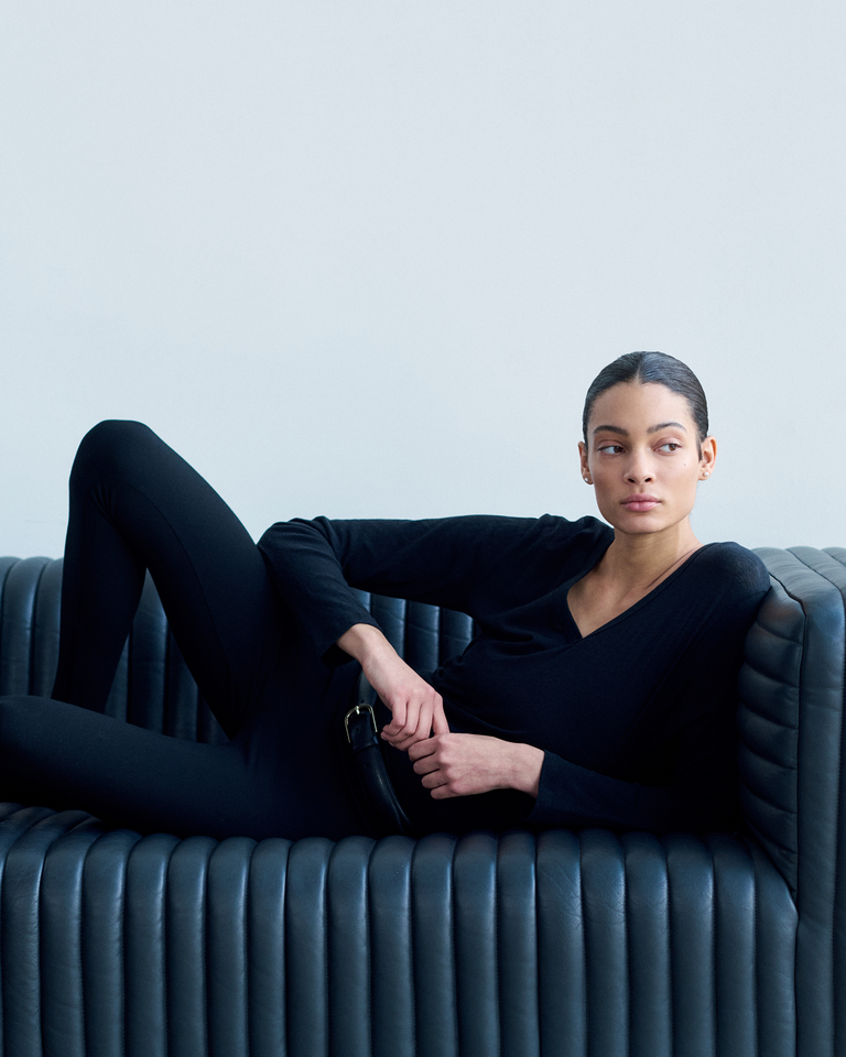 Woman leaning on couch in stirrup leggings and black long sleeve tee.