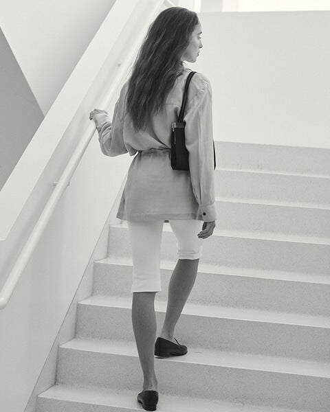 Woman leaning down in black heels with floral jacket, holding bag.