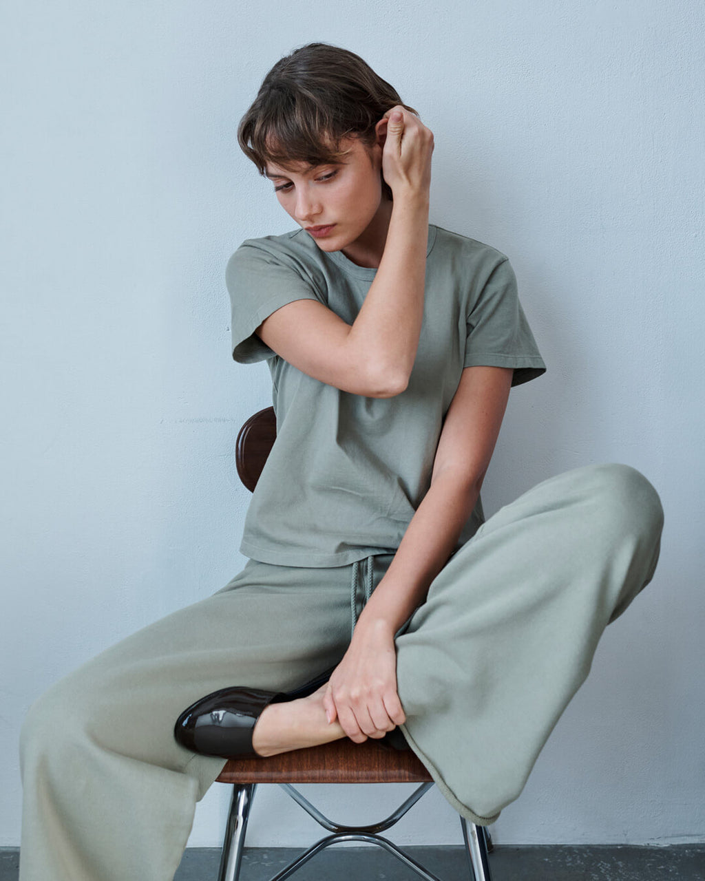 Woman in chair leaning against table in barb satin pacific dress, hand in hair