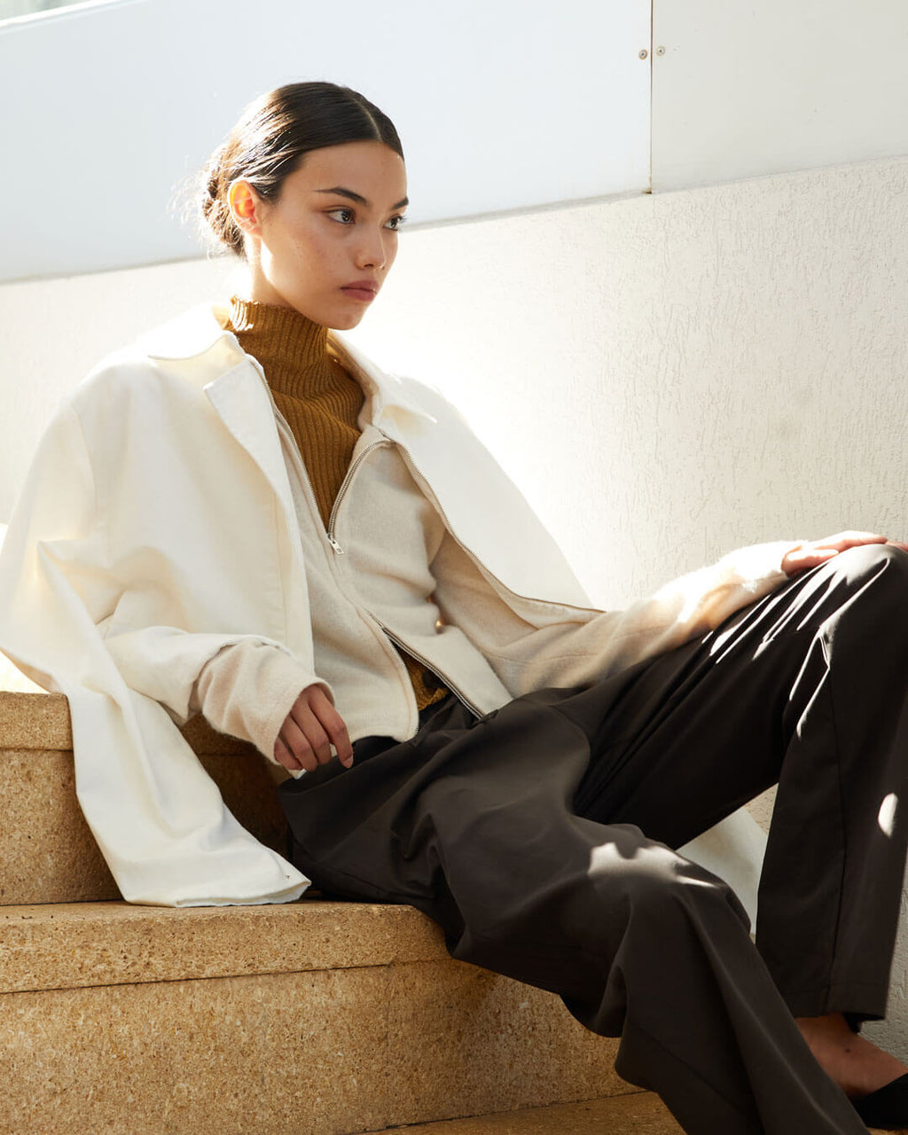Woman sitting on steps with brown trousers, cardigan, turtleneck and zip up jacket
