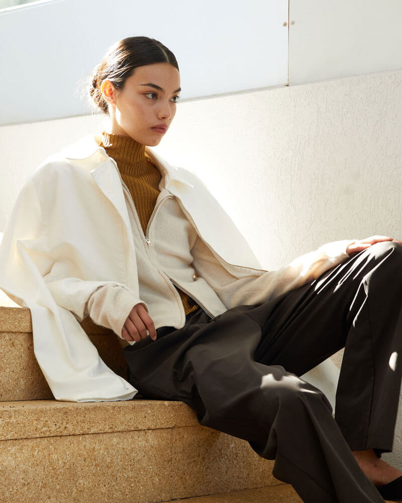 Woman sitting on steps with brown trousers, cardigan, turtleneck and zip up jacket