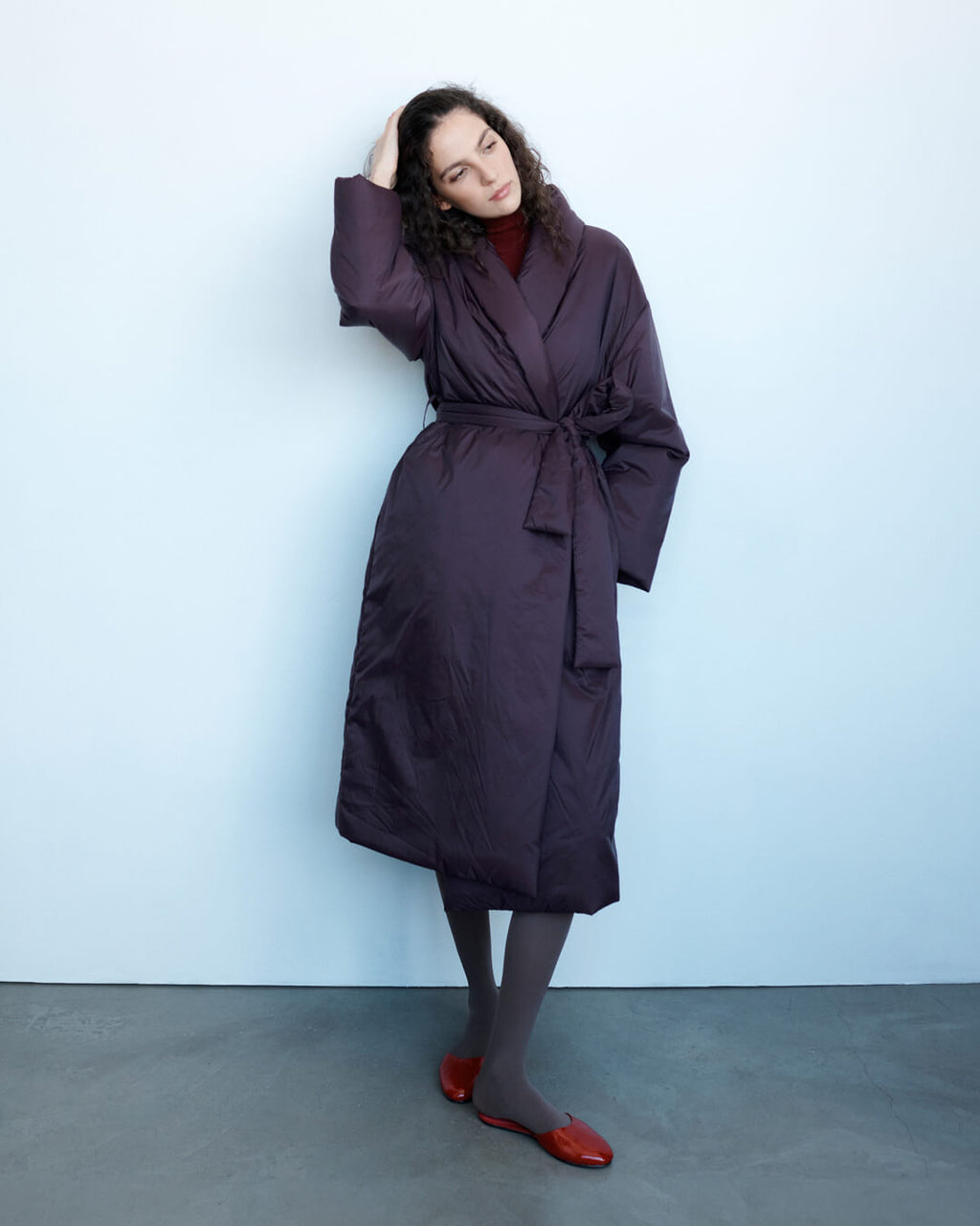 Woman leaning against wall in Bo trench with tights and ruby romy mules