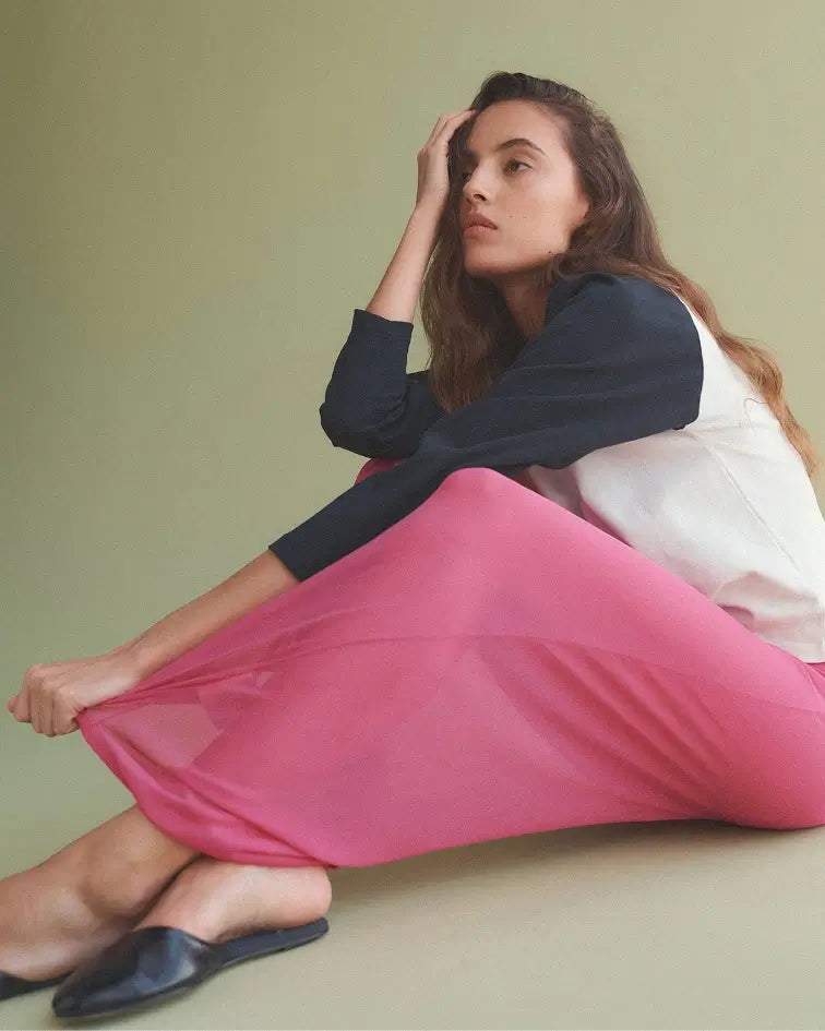 Woman sitting down in pink midi skirt and baseball tee.