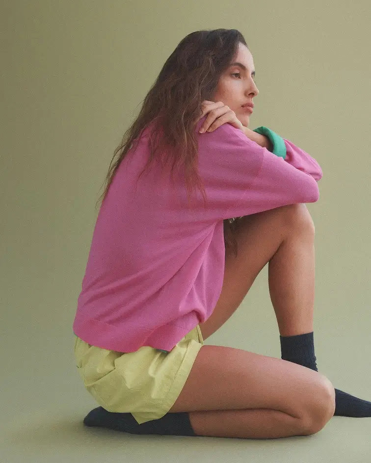 Woman sitting down in pink midi skirt and baseball tee.