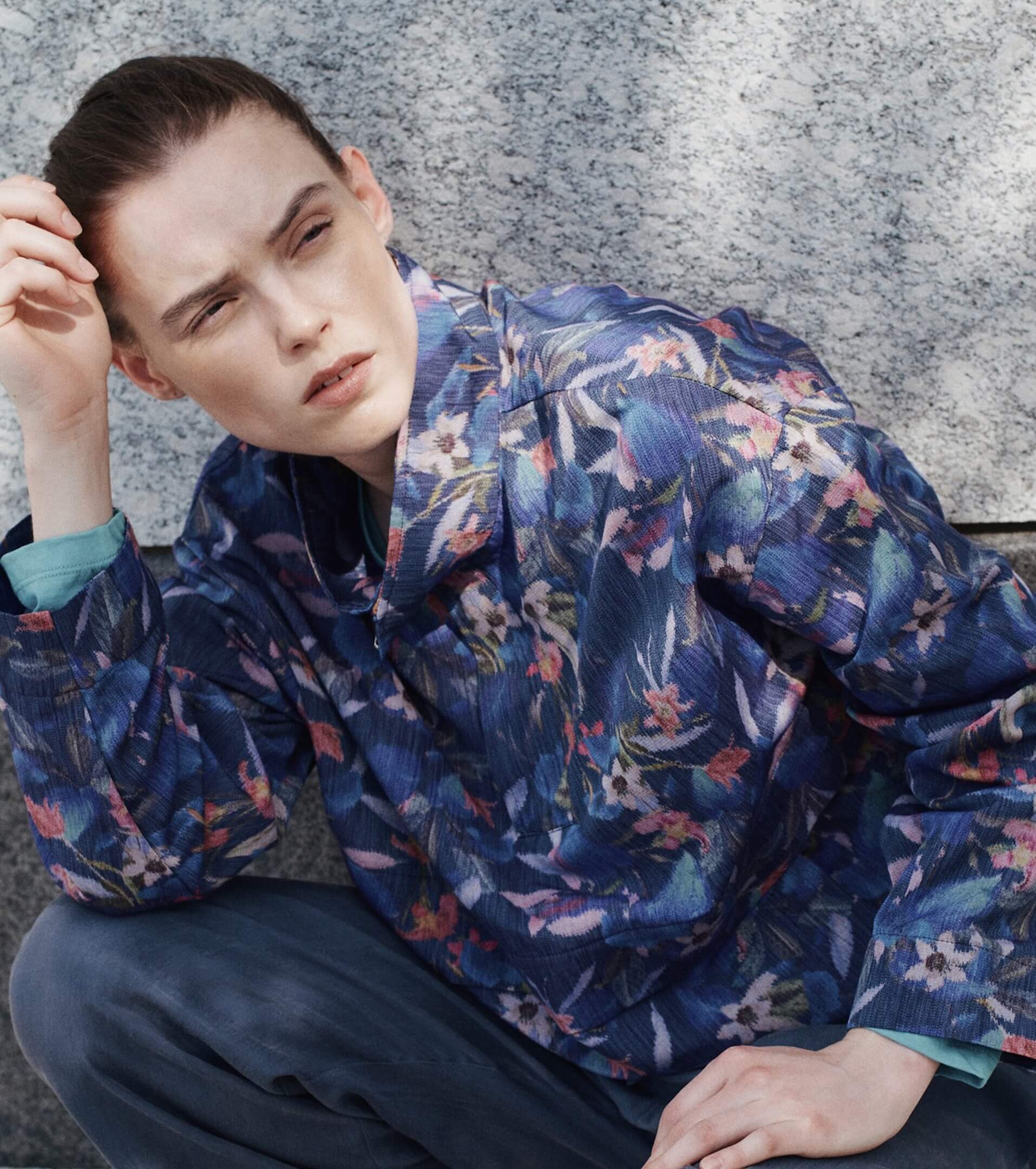 Woman kneeling down in front of wall in floral anorak.