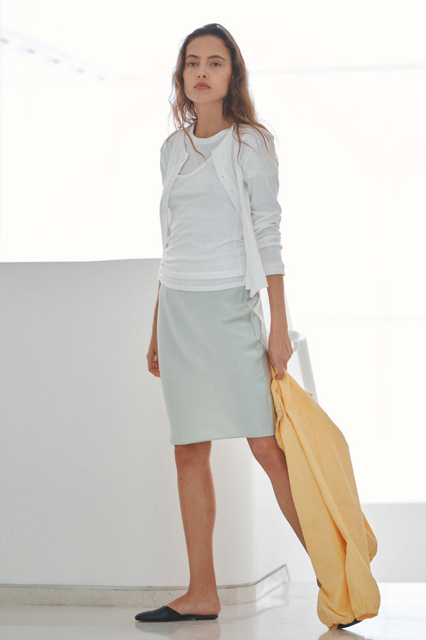 Woman standing in watercress slip skirt with white layered tank over cardigan and t-shirt, with white background.