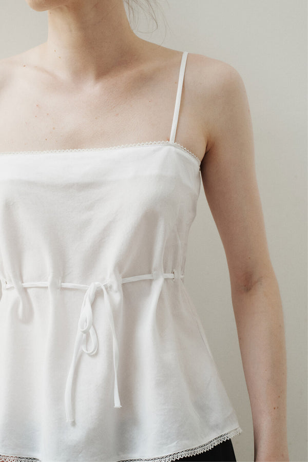 Close up of white Yoko lace top in front of blank wall.