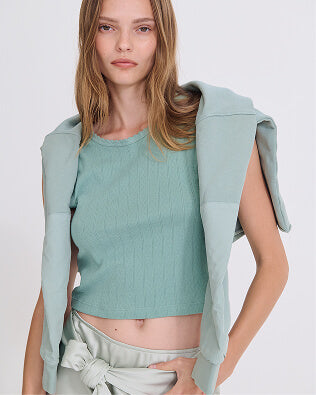 Woman walking forward carrying books, in front of glass window with city view, wearing crop trousers with black flats and white and black long sleeve tshirt.