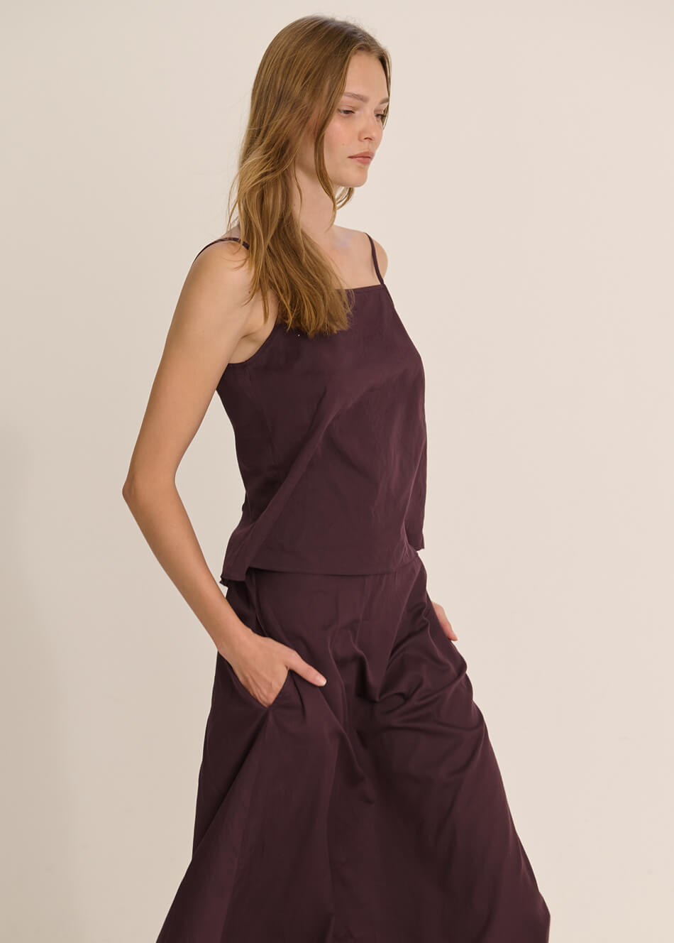 Model is wearing burgundy tank and skirt in front of white wall