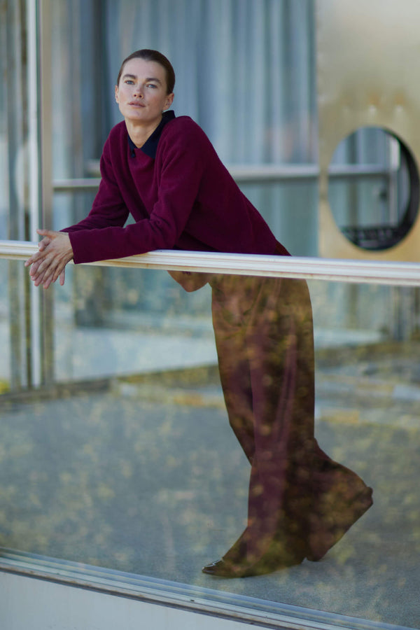 Woman leaning against balcony rail in mulberry pullover and bordeaux pant
