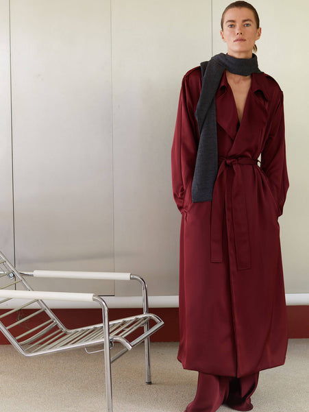Woman standing in Barb trench bordeaux and charcoal grey james as scarf next to a chair