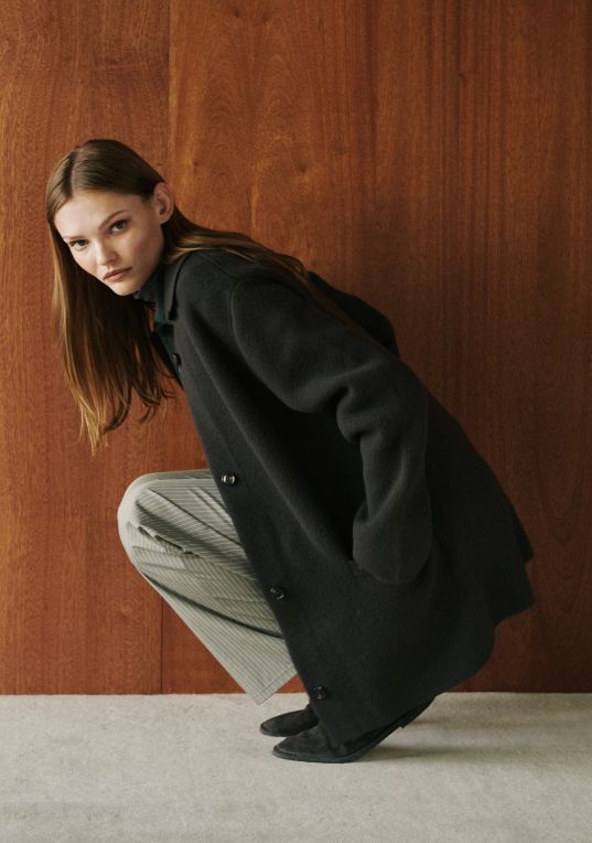 Model is squatting down in zoe sweater jacket and pinstripe pants.
