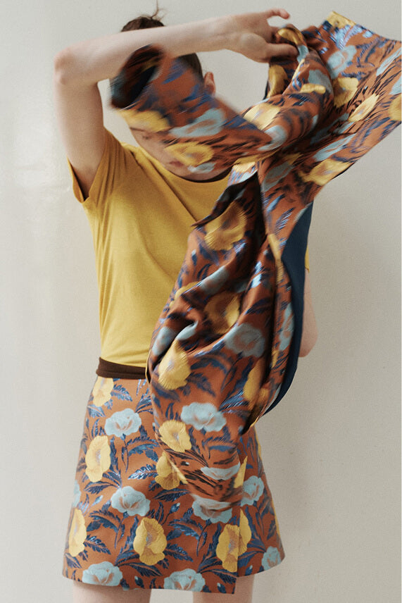 Close up of Pam floral set and yellow tee. Jacket being thrown over, in front of blank wall.