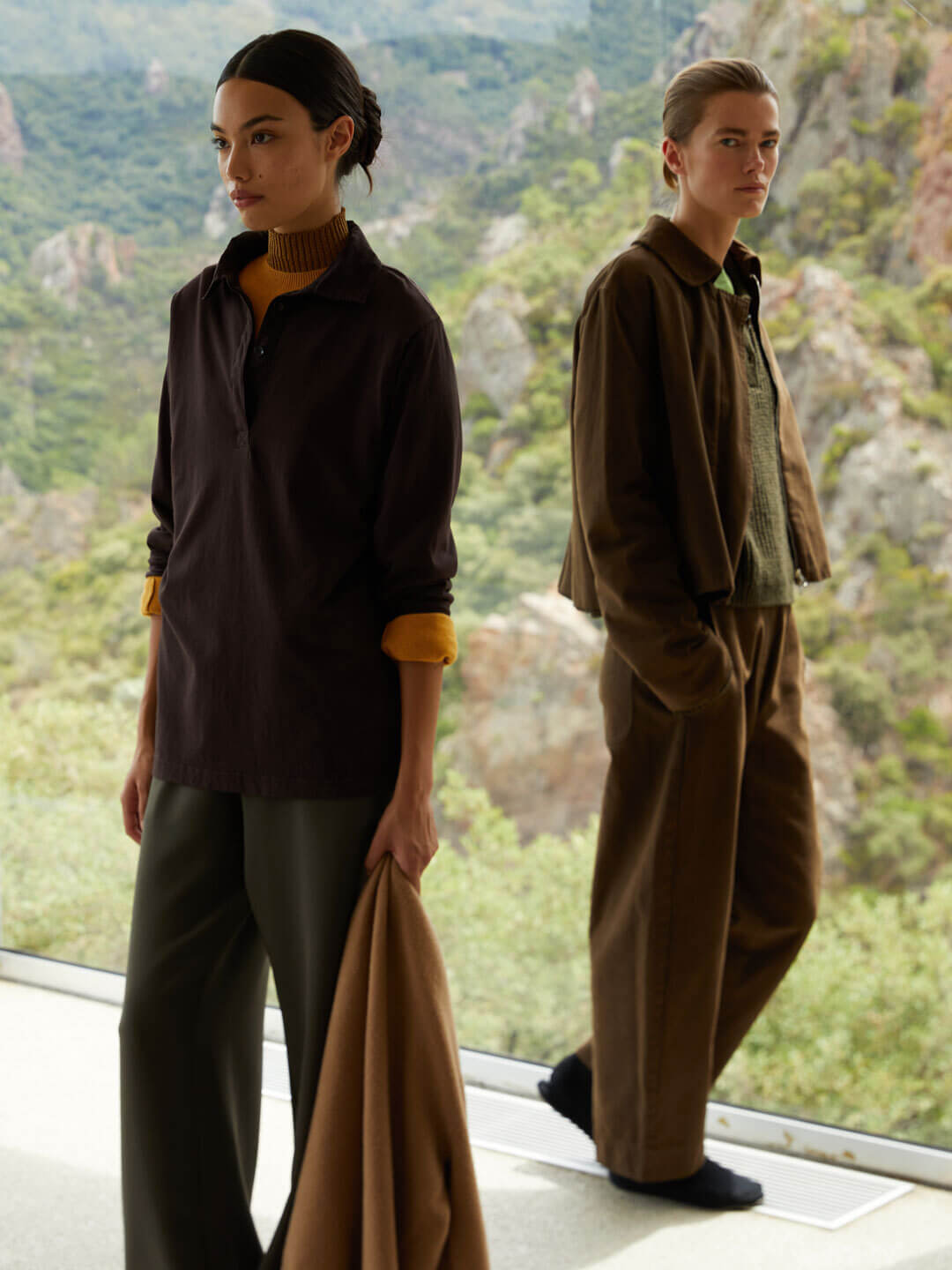 Two women in fall clothing in a house with a large window posing