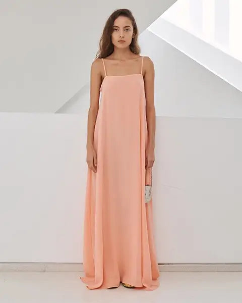 Woman standing with white background, in peach maxi dress.