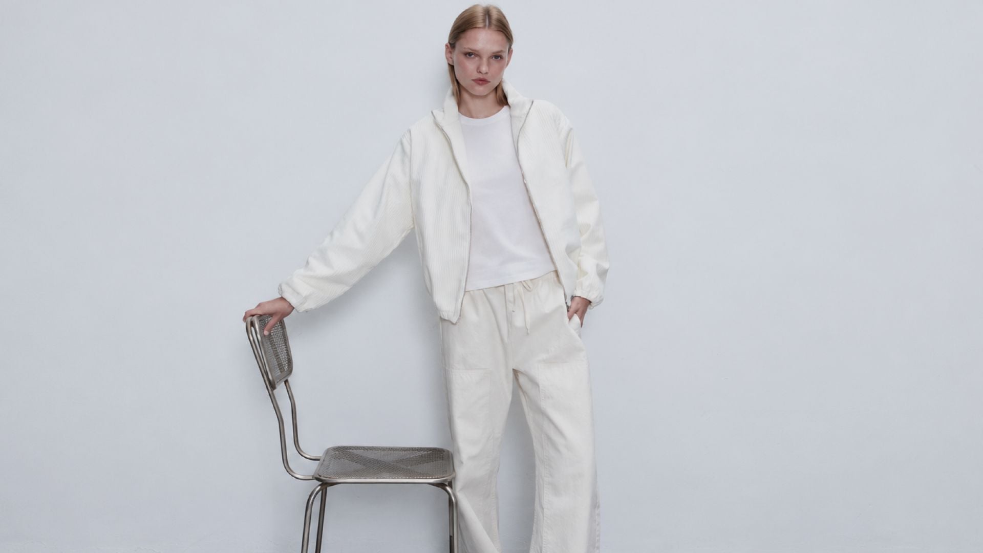 Model is standing holding metal chair in white tee and sammi corduroy set in creme.