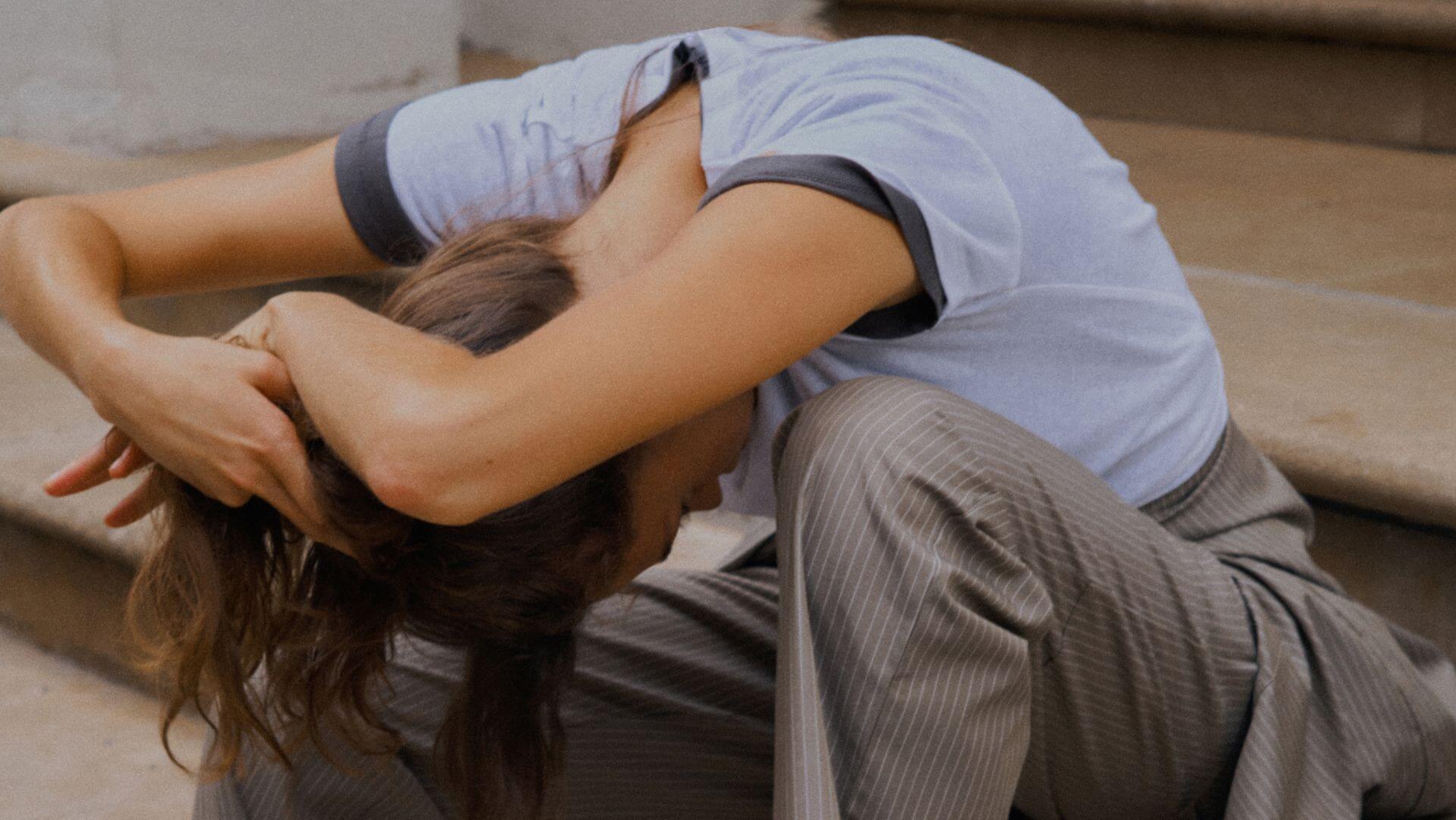 Model is leaning down with hands over head on steps, wearing t-shirt and pinstripe pants.