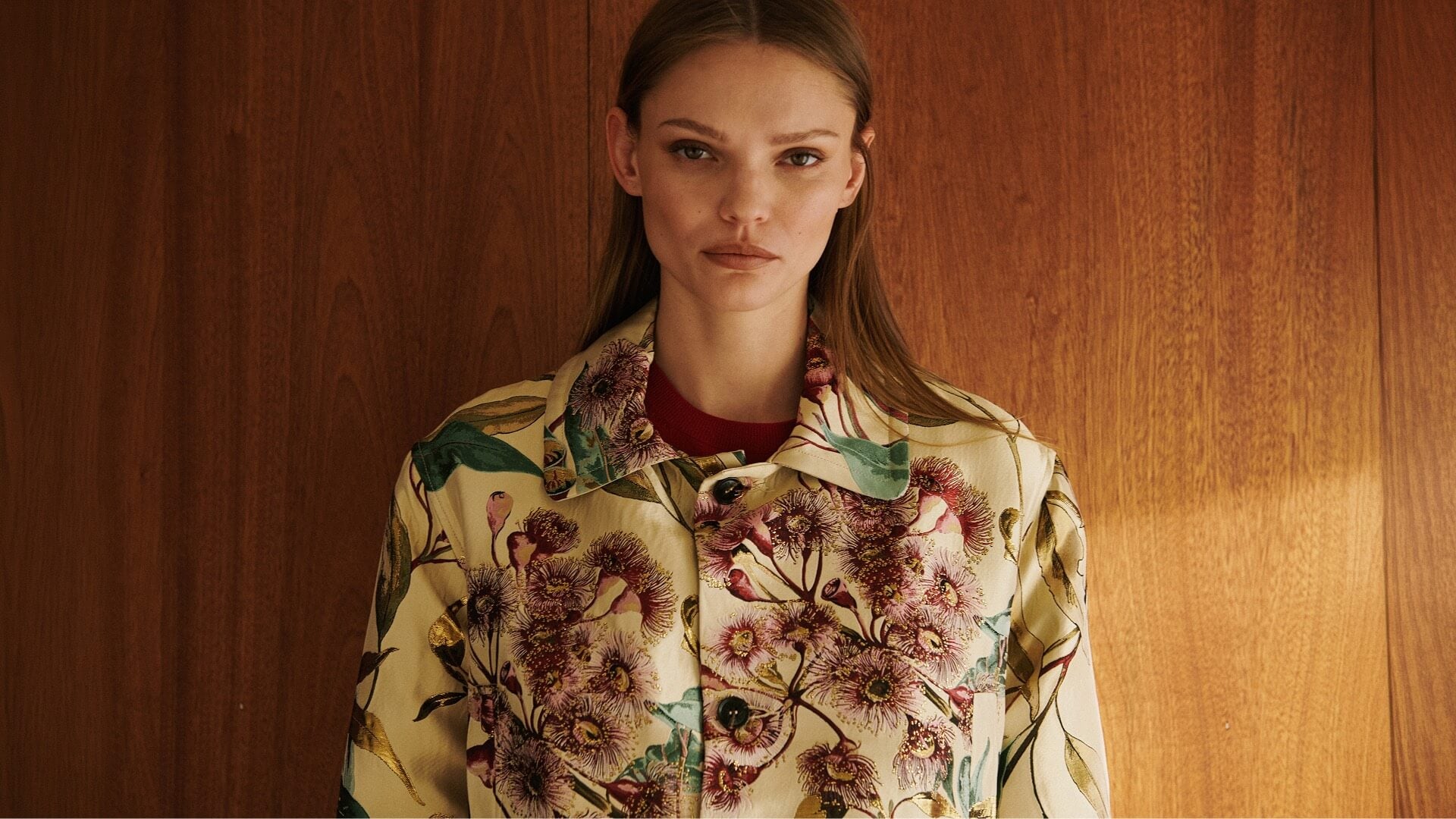Model is wearing floral jacket in front of wooden wall