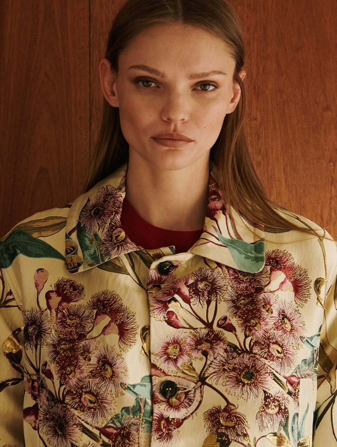 Model is wearing floral jacket in front of wooden wall