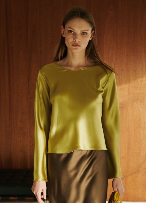 Model is standing in barb satin chartreuse long sleeve with brown satin skirt.