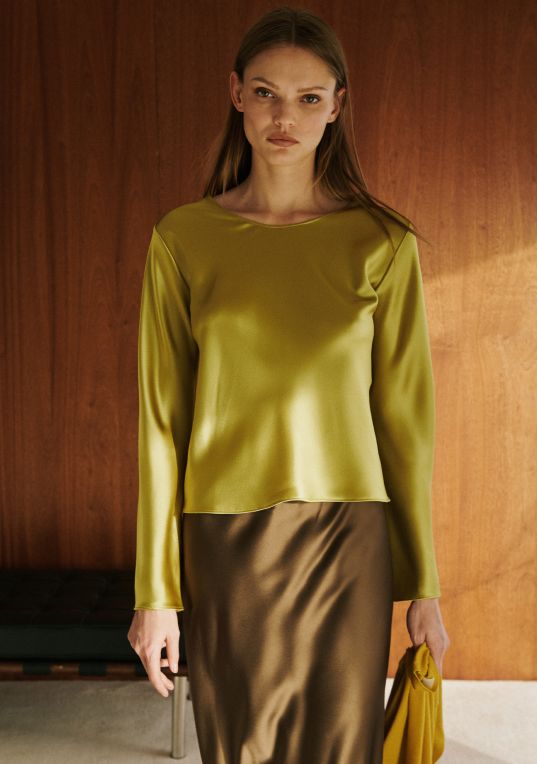 Model is standing in barb satin chartreuse long sleeve with brown satin skirt.