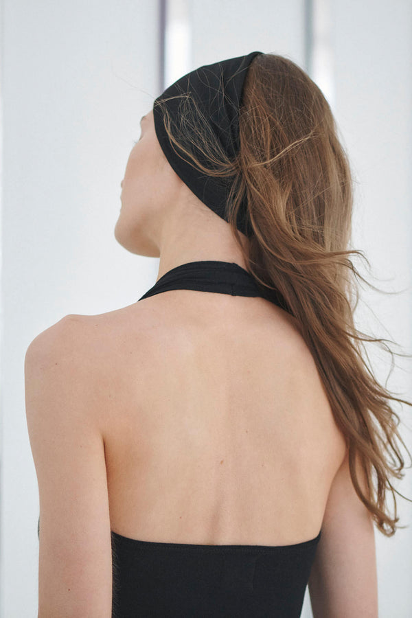 back of woman in black headband with halter top, white background.