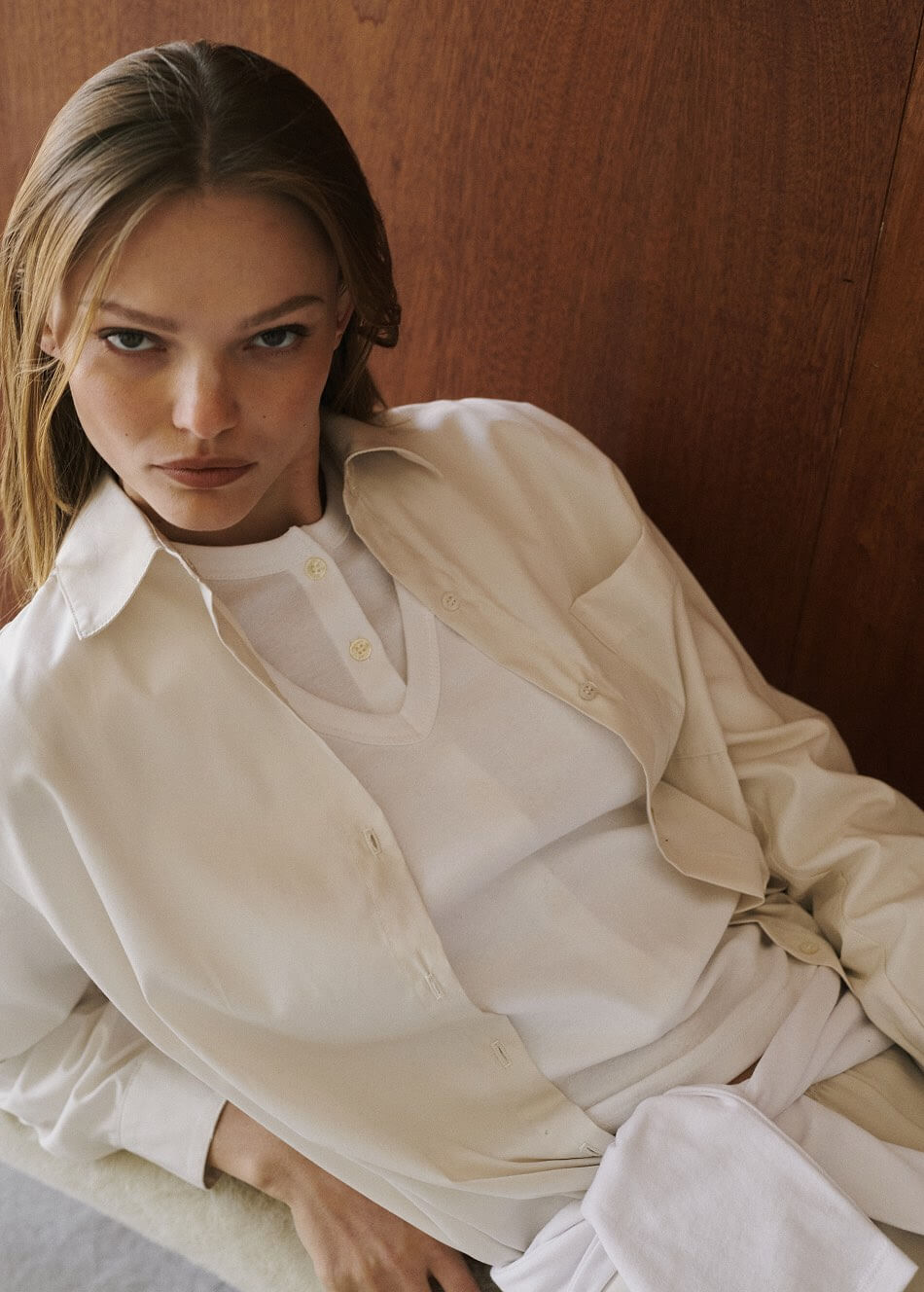 Close up of woman leaning down wearing white v neck layered over button down, with beige button down.