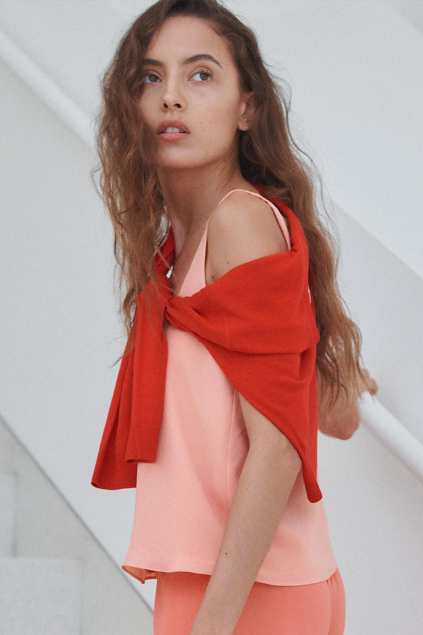Woman looking to the side in peach colored tank with red sweater draped over.
