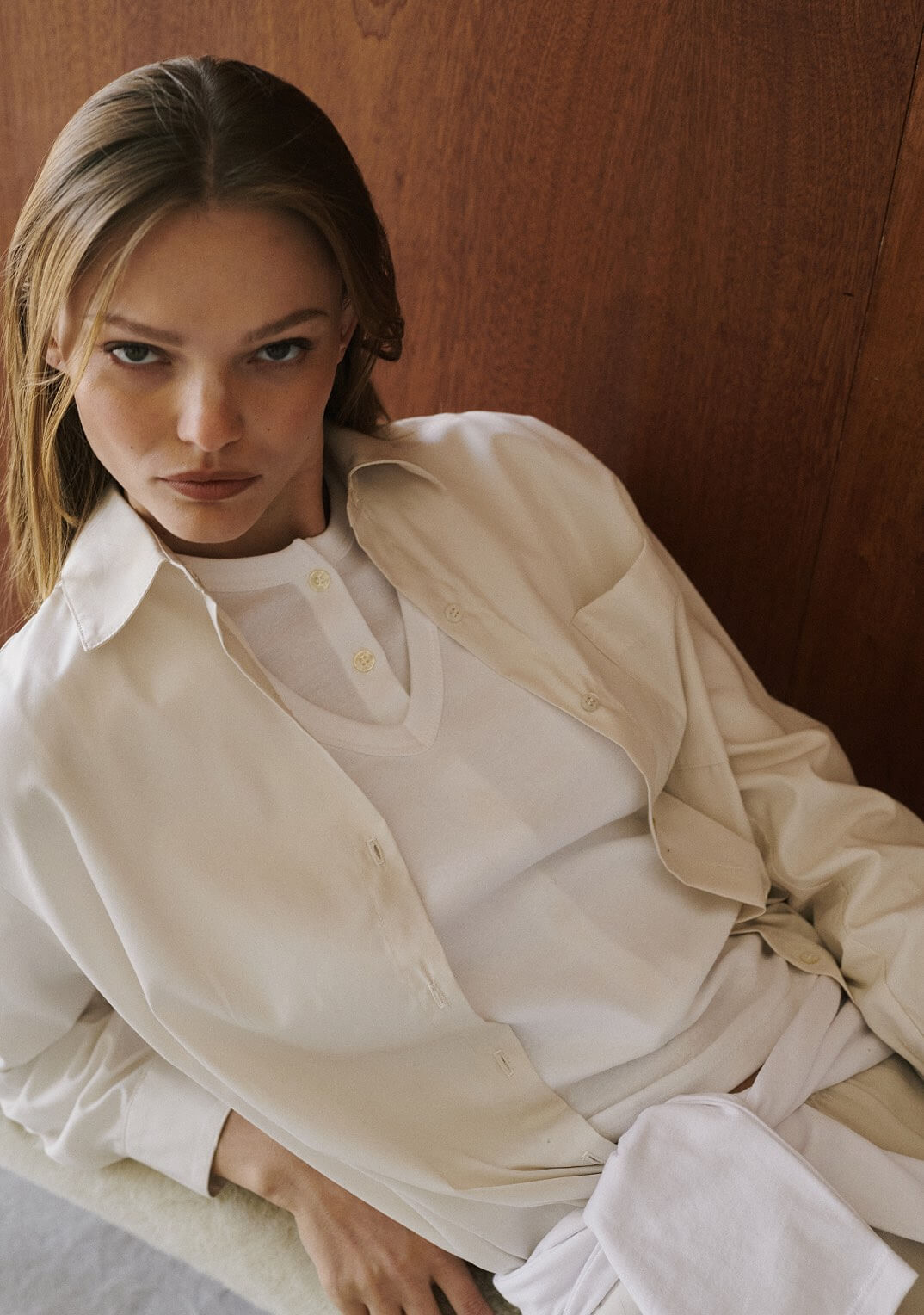 Close up of woman leaning down wearing white v neck layered over button down, with beige button down.