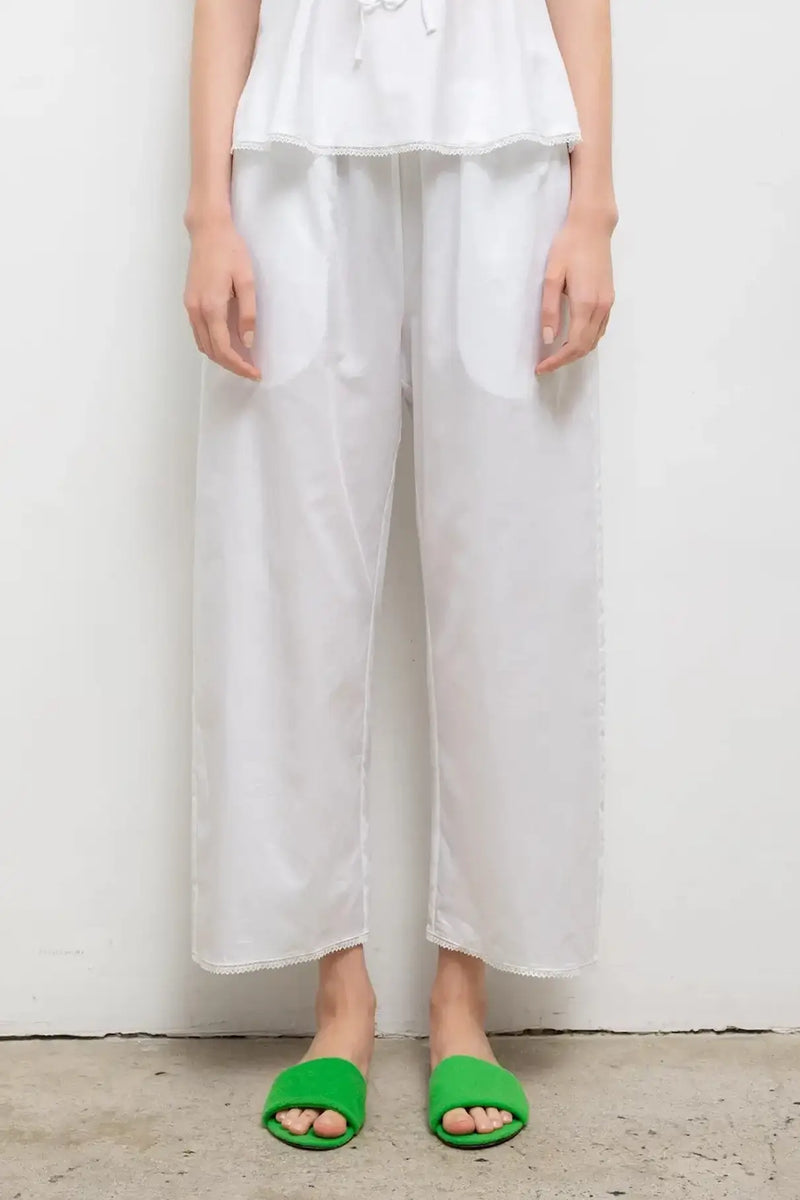Close up of white yoko lace crop pants on model with green slides.