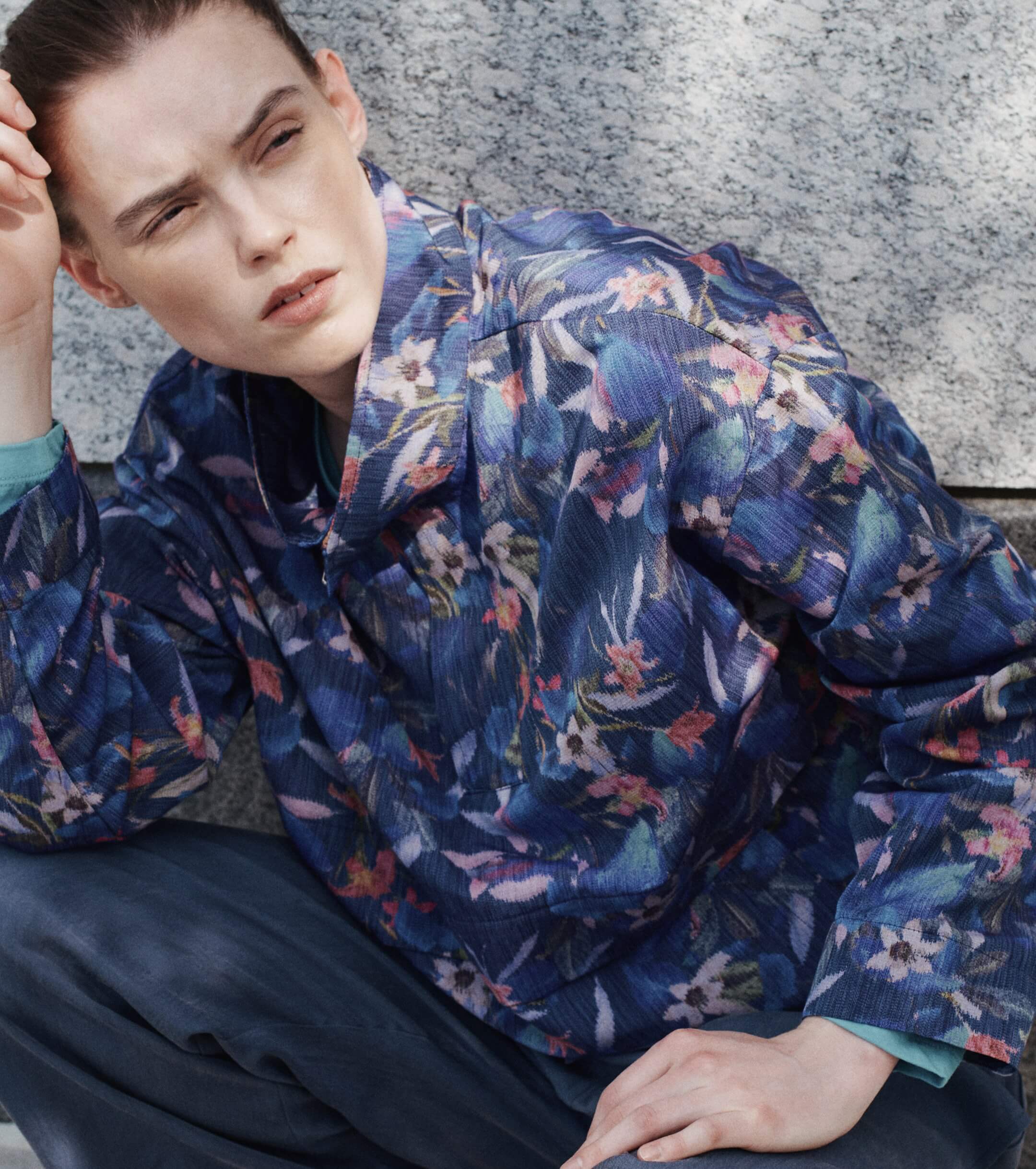 Woman kneeling down in front of wall in floral anorak.